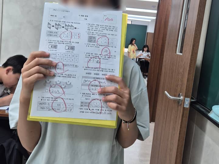 한맥학원 로고 앞에서 수학 100점, 영어 100점 시험지를 든 학생