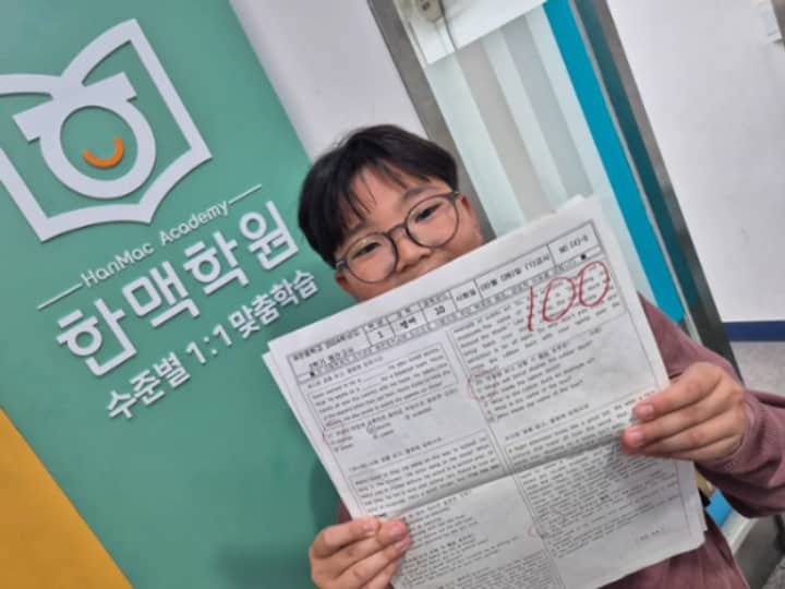 한맥학원 로고 앞에서 100점 시험지를 든 학생